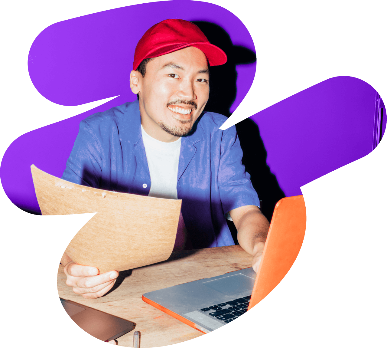 a man wearing a red hat is holding a piece of paper in front of a laptop