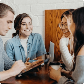 a group of people are sitting around a table with a laptop and a tablet .