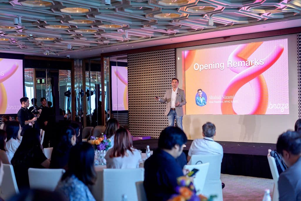 Man presenting 'Opening Remarks' on a large screen to an audience at a conference.