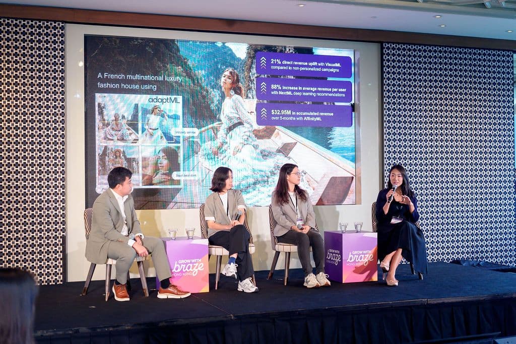 A panel of four speakers on stage in front of a screen displaying a presentation about AdoptML and Braze, featuring fashion images and performance data.