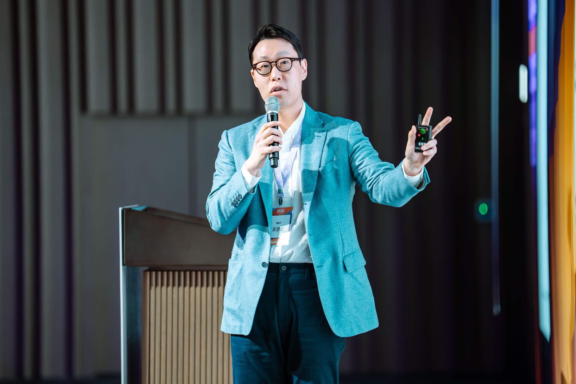 Man in a blue blazer speaking into a microphone, holding a presentation remote.