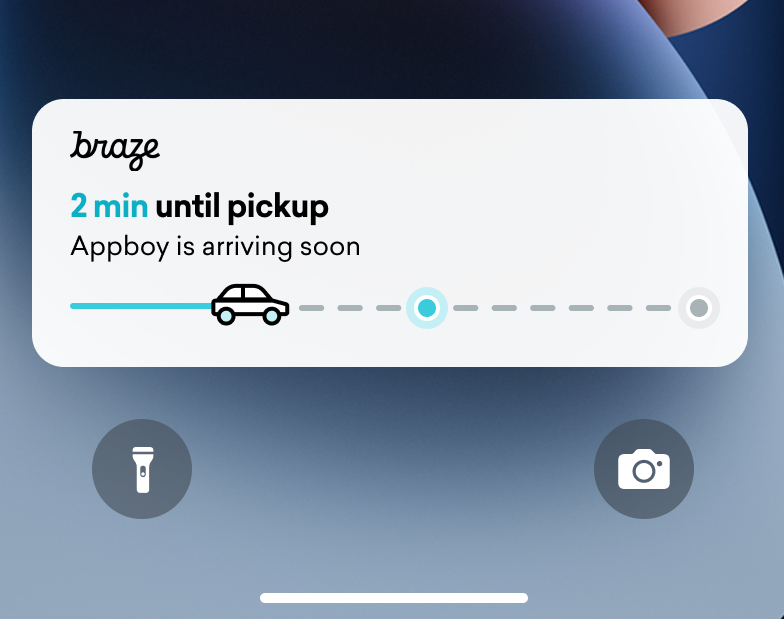 Un suivi de livraison d’activité en direct sur l’écran de verrouillage d’un iPhone. Une barre d’état avec une voiture est presque à moitié remplie. Le texte indique « 2 min jusqu’à la récupération »